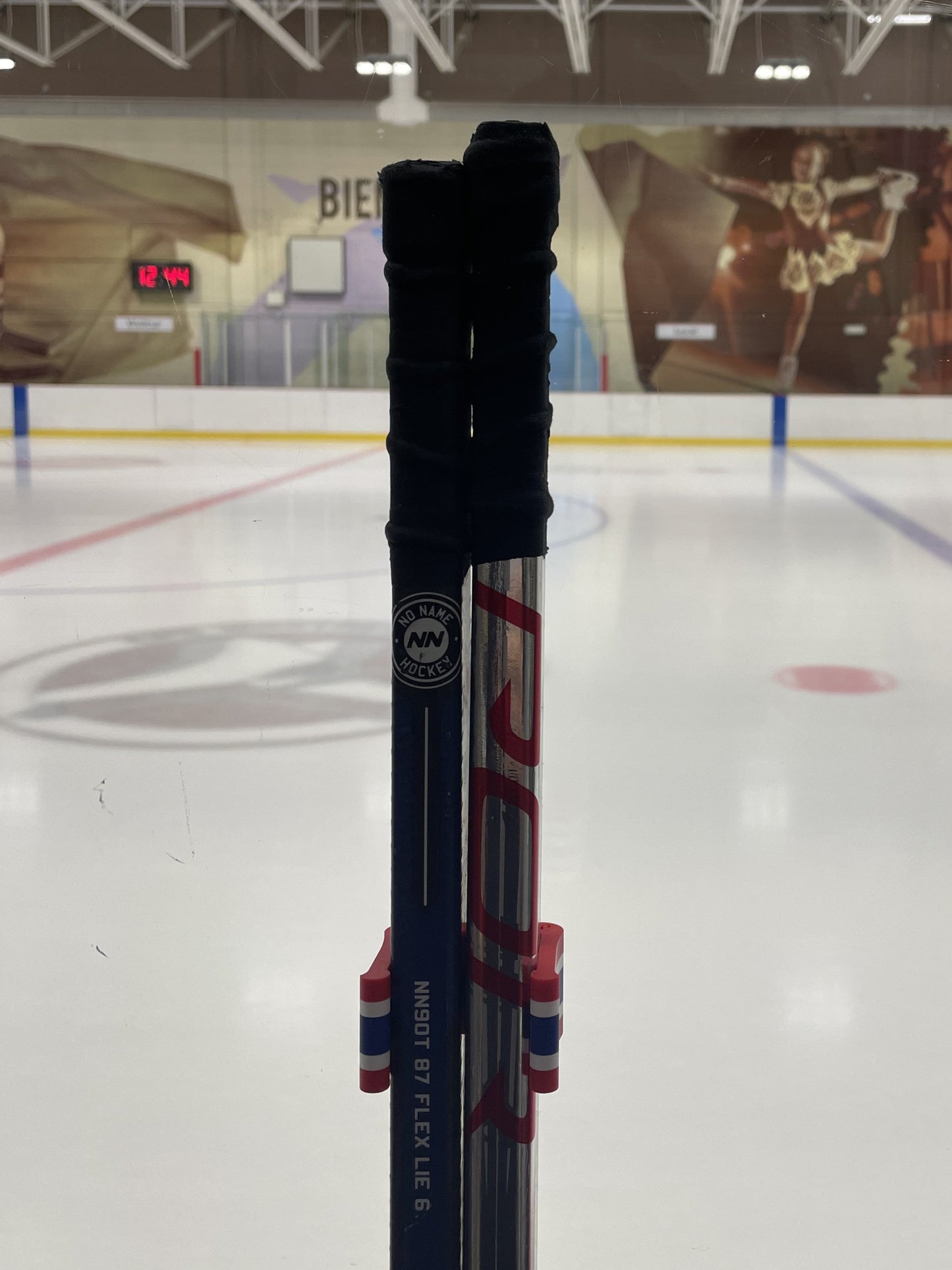 Stick Em Up Hockey Stick Clip Holding Two Sticks in Front of an Ice Rink