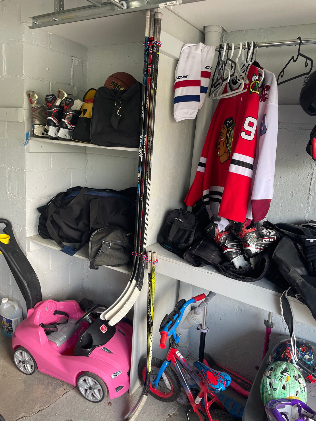 Hockey equipment organized in a garage. Sticks mounted, jerseys hanging, and skates airing out.