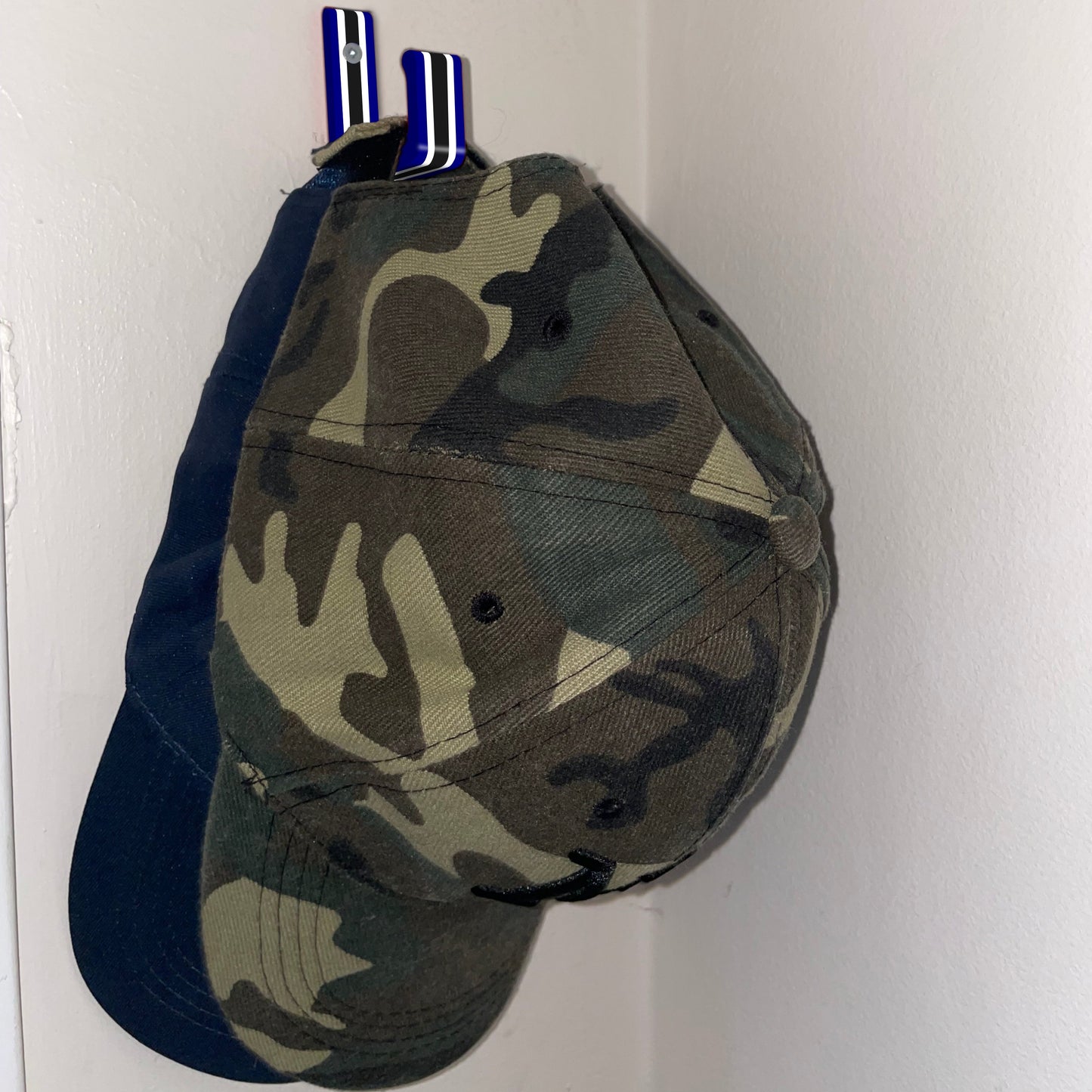 A navy, white and black Stick Em Up Baseball Cap Holder holding two caps shown from an isometric view