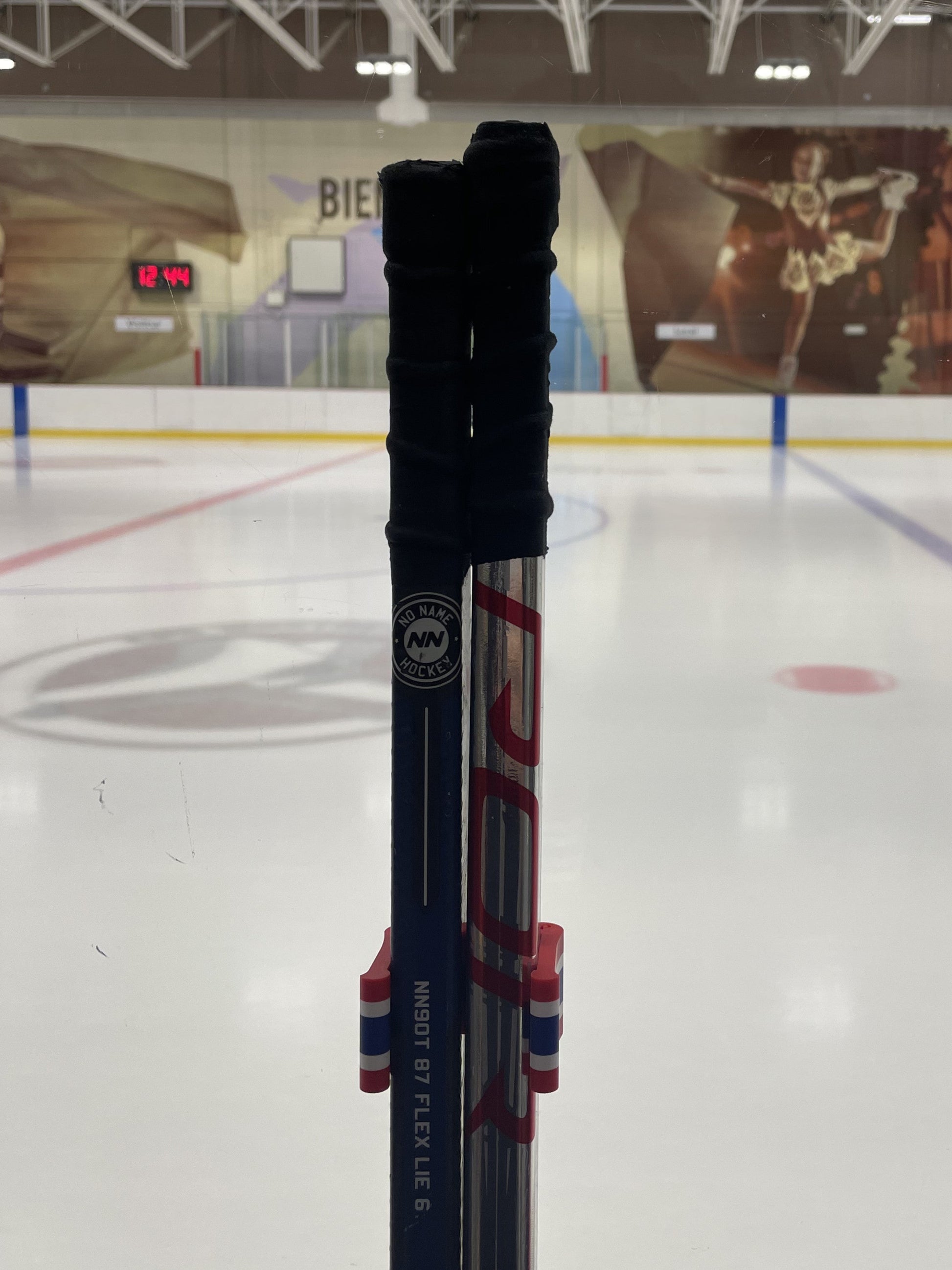 Stick Em Up Hockey Stick Clip Holding Two Sticks in Front of an Ice Rink