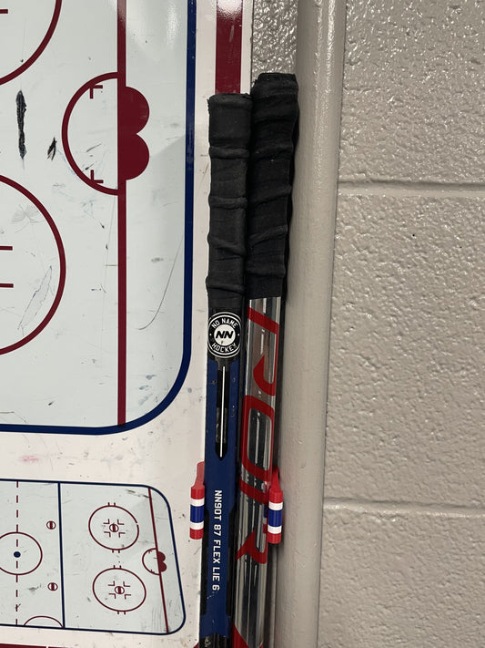 Stick Em Up Hockey Stick Clip Holding Two Sticks Aligned in Front of a Locker Room's Practice Board 