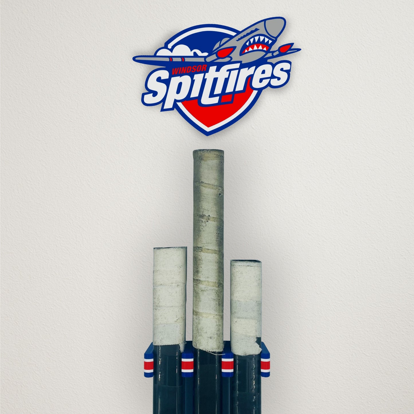 Three hockey sticks mounted in a Stick Em Up hockey stick wall mount with a 'Spitfires' Plaque of their logo above them 